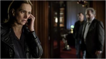 Vrouw heeft telefoon aan haar oor er er staan twee mannen in de achter grond.