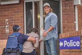 Detective Cormack houdt de deur open voor een man die gearresteerd wordt door een agent