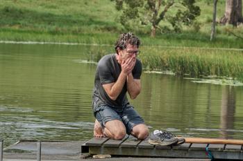 Een man zit doorweekt op zijn knieën op een stijger en heeft huilend zijn handen voor zijn mond