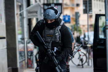 Politieagent in zware, beschermende kleding kijkt op zijn hoede en heeft een geweer vast