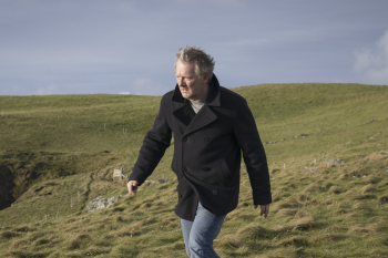 Detective Jimmy Perez uit Shetland loopt in de wind over een open heuvellandschap