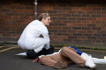 Een forensisch patholoog hurkt in een wit pak bij een lijk op de grond
