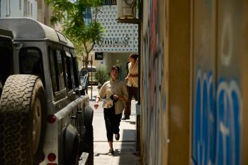 Vrouw loopt in zonnige straat langs geparkeerde auto en murale.