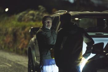 Twee mannen staan 's nachts naast een auto op een donkere weg.