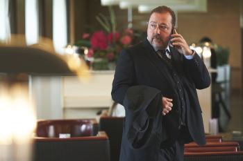 Man in pak voert telefoongesprek in restaurant, houdt jas vast.