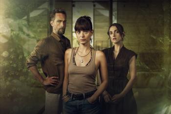 Drie personen met serieuze blikken in een wazige achtergrond, een man en twee vrouwen.