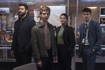 Vier mensen in businesskleding in een kantooromgeving, met foto's op de achtergrond.