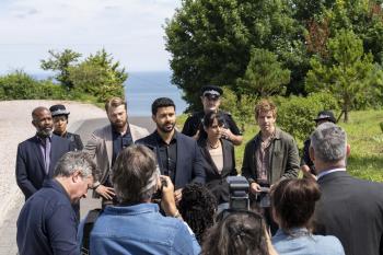 Groep mensen houdt een persconferentie buiten, met bomen en zee op de achtergrond.