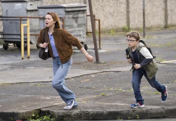 Vrouw en jongen rennen op parkeerplaats, kijken gehaast.