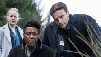 Drie mensen kijken geconcentreerd naar iets buiten.