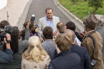 Man in licht pak spreekt buiten met journalisten en fotografen.