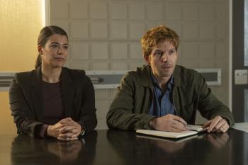 Twee mensen aan tafel, man met notitieboek, vrouw kijkt geïnteresseerd.