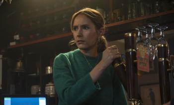 Vrouw in groene trui tapt bier in een bar, kijkt bezorgd.