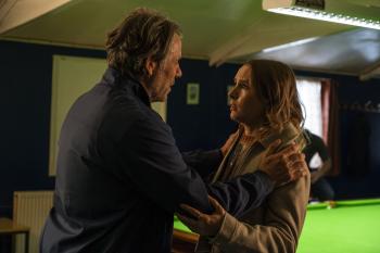 Twee mensen praten emotioneel in een kamer met een groene biljarttafel.