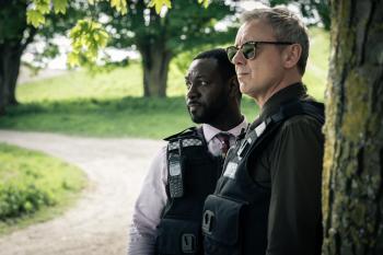 Twee mannen in politie-uniform kijken waakzaam, buiten bij een boom.