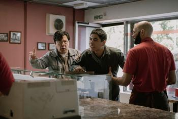 Mensen discussiëren in een winkel, twee klanten tegen een medewerker in rood shirt.