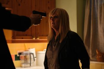 Persoon met pistool richt op vrouw in keuken, gespannen sfeer.