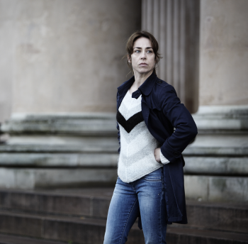 Vrouw in blauwe jas staat voor klassieke stenen kolommen.