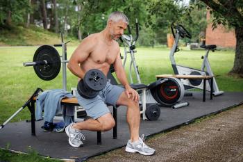 Man doet bicep curls met halter in buitenfitnessruimte.