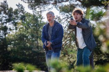 Twee mannen in een bos houden een pistool in de hand, alert kijkend.