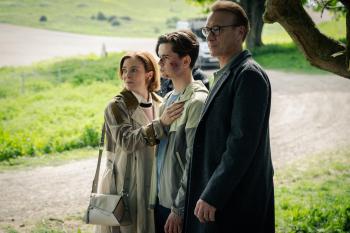 Drie mensen staan buiten bij een boom in een groene omgeving, kijken bezorgd.