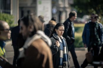 Vrouw met sjaal loopt op drukke straat met onscherpe mensen op achtergrond.