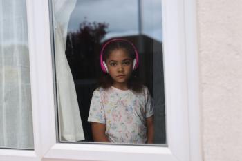 Meisje met roze koptelefoon kijkt ernstig uit het raam.