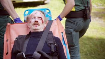 Man op brancard met wonden, begeleid door hulpverleners buiten.