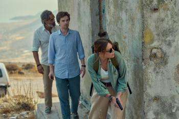 Drie mensen buiten bij een verouderd gebouw; één vrouw houdt een pistool vast.