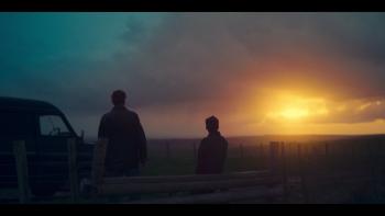 Twee personen staan bij een hek, kijken naar zonsondergang.