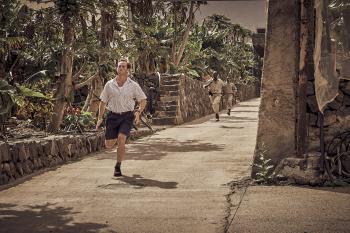 Man in witte overhemd rent op smalle zonnige straat.