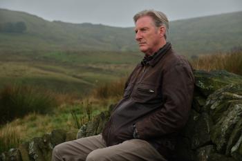 Oude man zit in het ruige Britse landschap