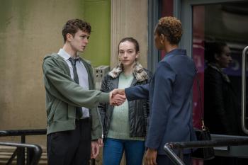 Twee mensen schudden elkaar de hand, een vrouw kijkt gespannen toe