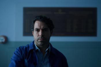 Serieus kijkende man met zwart haar in schemerige ruimte 