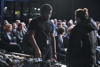 Een man en vrouw praten met elkaar in een donkere zaal met explosieven op tafel