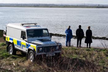 Politievoertuig bij rivier, drie mensen kijken over het water.