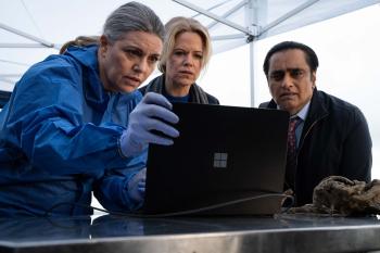 Drie personen kijken naar een laptop onder een witte tent, vermoedelijk tijdens een onderzoek.