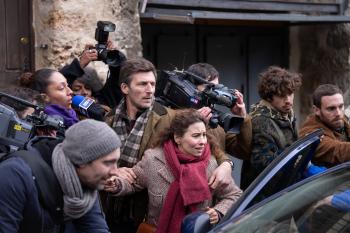 Een menigte van journalisten met camera's stormt op een auto af