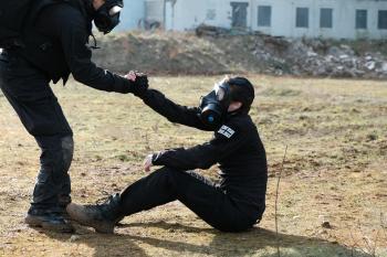 Een man in een zwart pak met gasmasker helpt een andere man overeind