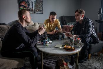 Drie jongens zitten geheimzinnig rondom een tafel 
