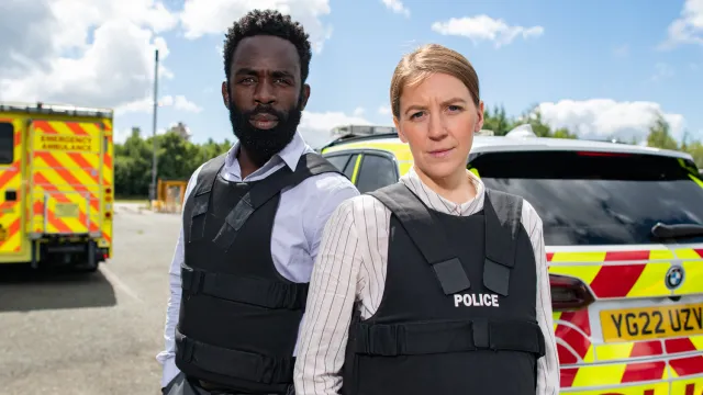 Twee politieagenten uit The Tower hebben hun handen in hun zakken en kijken naar de camera