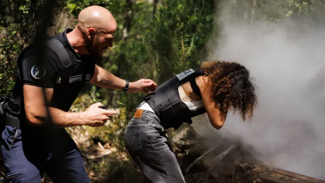 Twee mensen in beveiligingsuniform naast rook in een bosgebied.