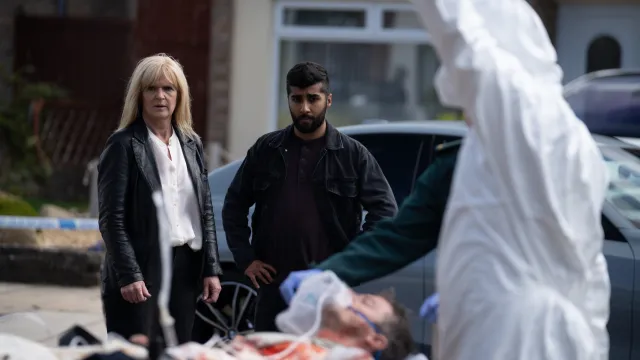 Vrouw en man kijken naar een gewonde op brancard, omgeven door hulpverleners.