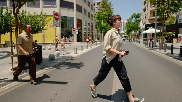 Twee mensen steken een zonnige straat over tussen moderne gebouwen.