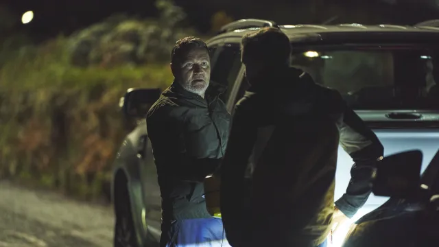 Twee mannen staan 's nachts naast een auto op een donkere weg.