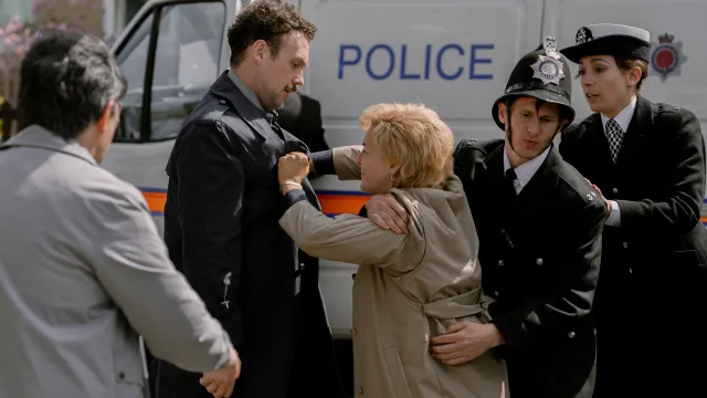 Politieagenten houden boze vrouw in beige jas tegen bij politiebus.