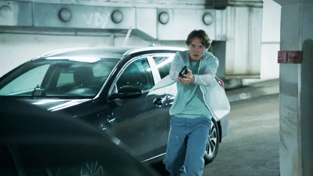 Persoon richt pistool in parkeergarage naast auto.