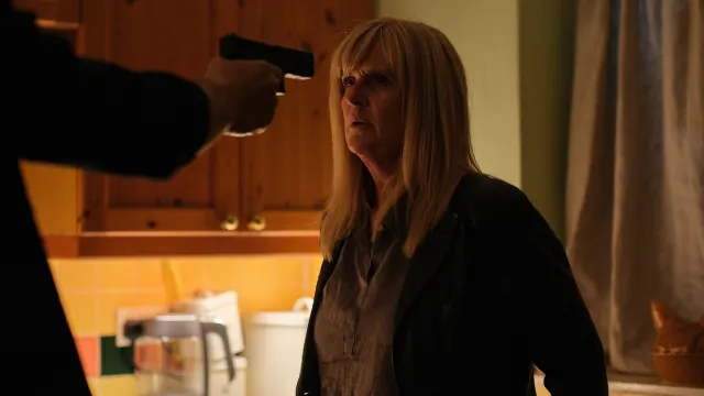 Persoon met pistool richt op vrouw in keuken, gespannen sfeer.