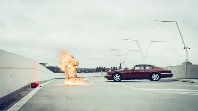 Rode auto op verlaten parkeergarage, met vlammen en een jerrycan op de grond.