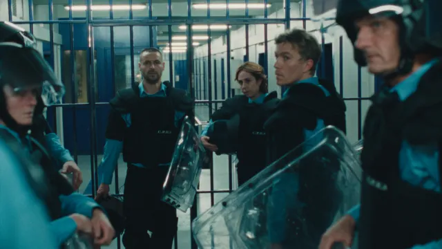 Beveiligers in uniform met schilden in een gang met tralies.